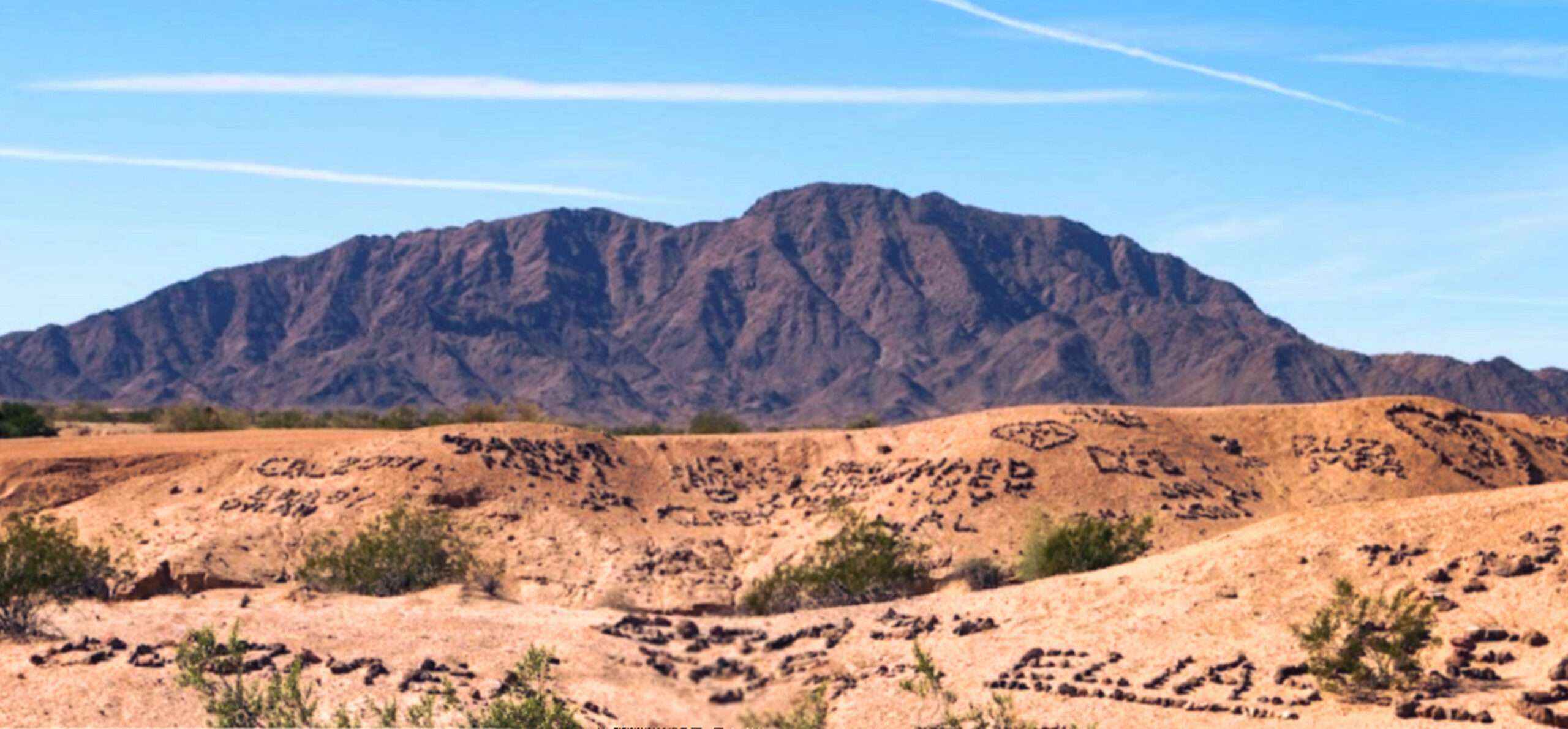 A photo of the Valley of the Names in California. The valley is covered in hard-packed Bentonite clay, and the earliest names are arranged using black lava rocks that stand in sharp contrast.