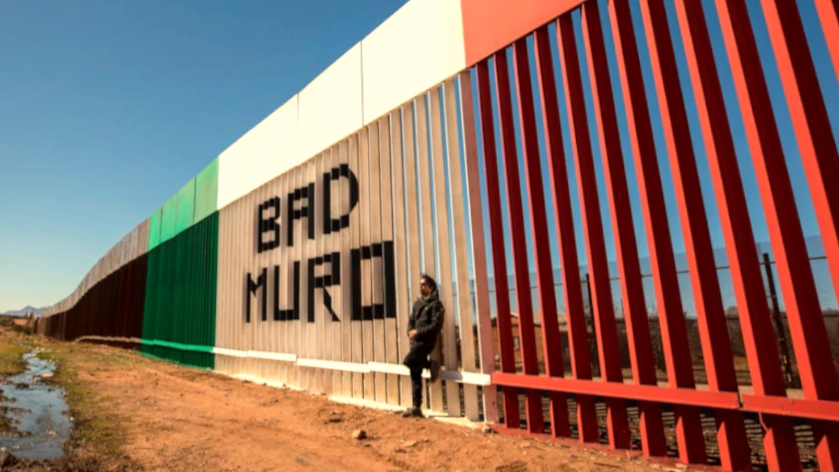 Man Standing against the Wall on the Border of USA and Mexico with a Sign "Bad Muro", Naco, Sonora, Mexico