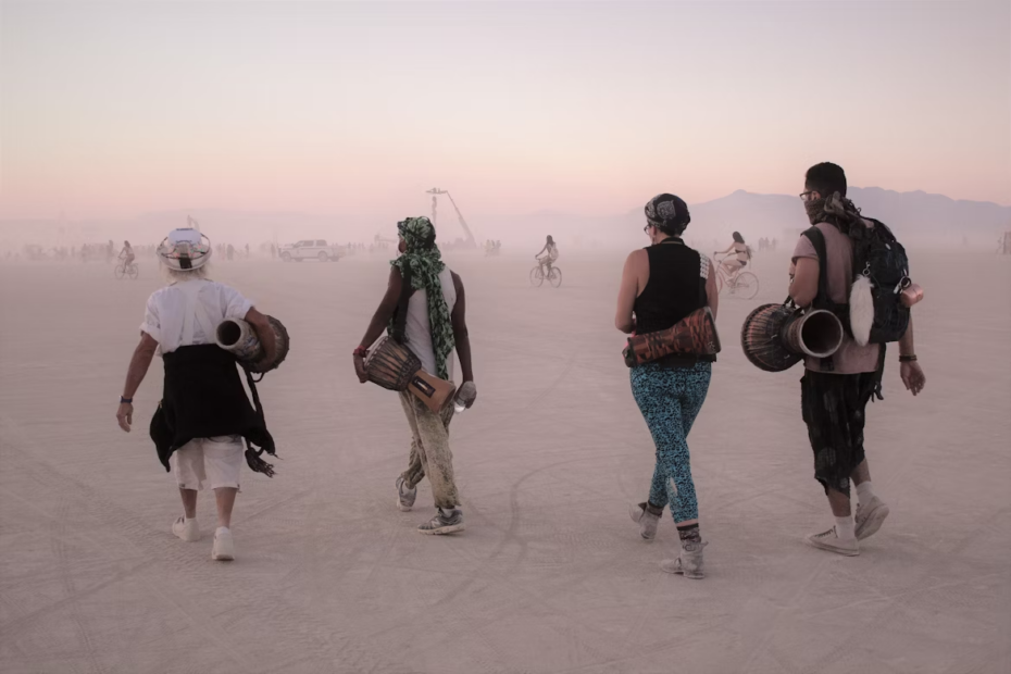 "Burners" carrying drums walk across the dusty Black Rock City in the Nevada desert as over 70,000 people prepare to gather for Burning Man 2025.
