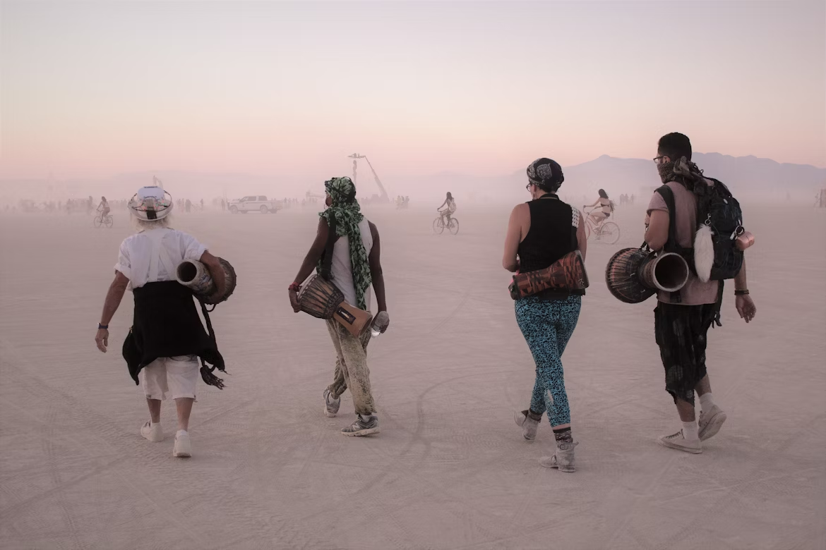 "Burners" carrying drums walk across the dusty Black Rock City in the Nevada desert as over 70,000 people prepare to gather for Burning Man 2025.
